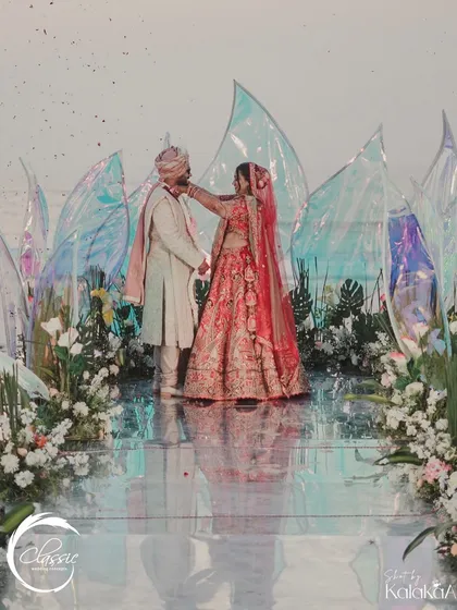 An intimate moment at the mandap. The translucent, crystal-like panels of the mandap create a dreamy, ethereal frame for the couple against the ocean backdrop.