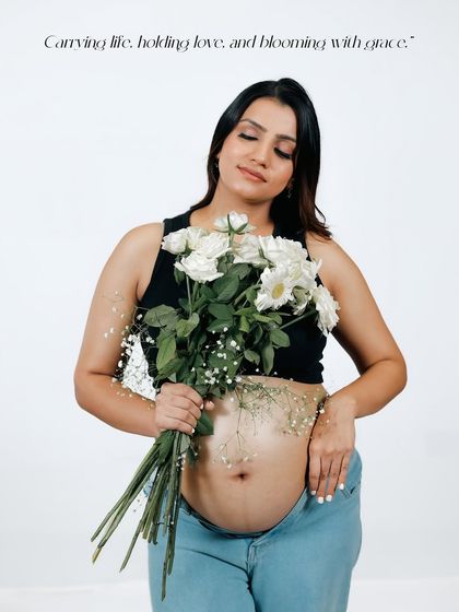 A beautiful and natural portrait of a mother-to-be in a casual black top and jeans. She holds a bouquet of white flowers, her bare bump blooming with life.