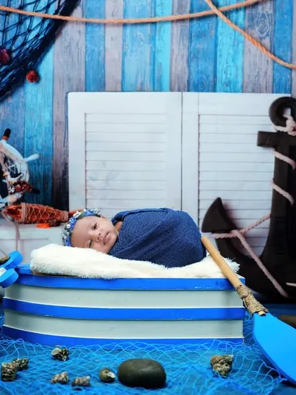 Ahoy, little sailor! This newborn is ready for a voyage in our nautical-themed setup, complete with an anchor, ship's wheel, and fishing nets.