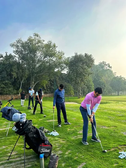 A group of golfers practicing on the grass tees as the sun begins to set.