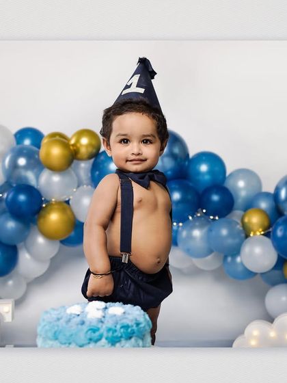 The birthday boy stands beside his cake, looking charming in his bow tie and suspenders before the smashing begins. The "ONE" marquee letters add a bright, celebratory feel to the studio setup.