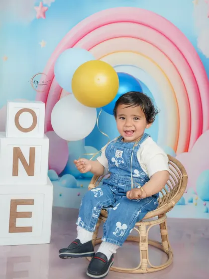 A cheerful first birthday portrait with a dreamy pastel rainbow backdrop, complete with "ONE" blocks and colorful balloons.