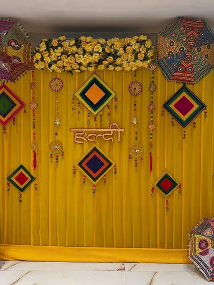 A clean and colorful haldi backdrop inside a banquet hall. The setup uses yellow drapes, Rajasthani umbrellas, and traditional hangings for a festive look.
