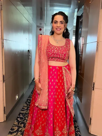 A full-length photo of a client in a vibrant pink and red lehenga. The makeup is fresh and radiant, perfect for a pre-wedding event or as a guest.