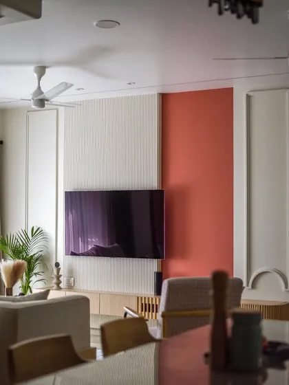 The living room features a TV wall with a mix of fluted panels and a bold coral accent color. The design is simple yet impactful.