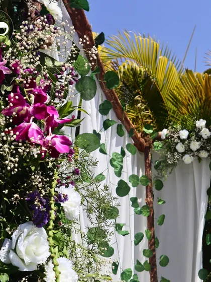 A detailed shot of the floral decor, showing the rich textures of purple orchids, white roses, and delicate baby's breath against a backdrop of green leaves and palm fronds.
