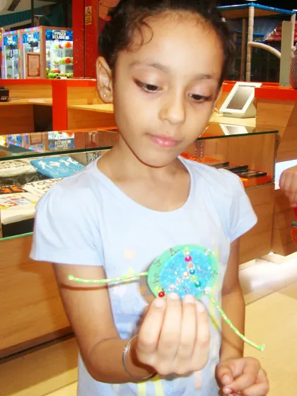 A girl carefully adds the finishing touches to her handmade rakhi, a perfect example of the creative fun at our workshops.