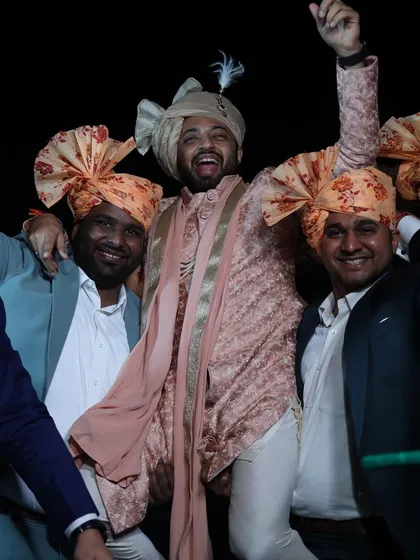 The groom and his squad, all smiles during the baraat. His custom-styled peach sherwani and beige safa stand out, while his friends wear coordinated floral pagdis.