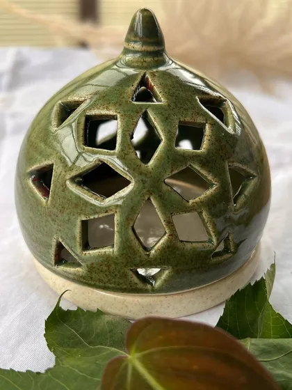 This olive green tea light holder has a mix of diamond and square cutouts. It's a modern take on a traditional lamp.