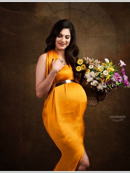 A soft and gentle portrait against a classic brown backdrop. The client, in a mustard gown, holds a basket of flowers, creating a warm and timeless maternity photo.