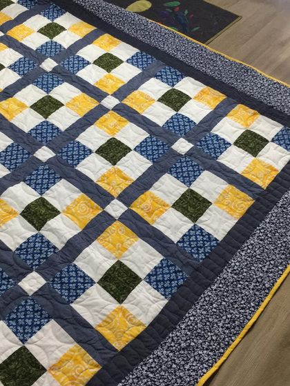 A classic "nine patch" quilt with a windowpane effect, in a calming blue, yellow, and green color scheme.