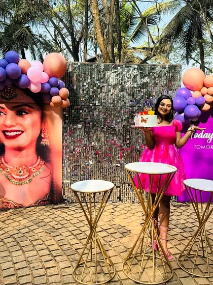 A chic outdoor 'Bride to be' celebration. This setup includes a sparkling silver shimmer wall, a life-sized personalized photo cutout of the bride, and a beautiful balloon arrangement in shades of pink and purple.