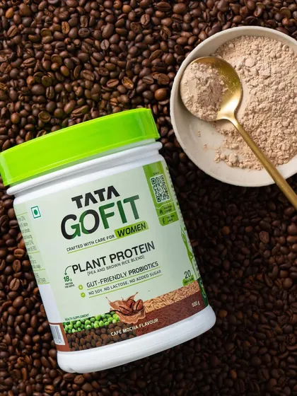 A rich, textured flat lay with the Tata GoFit protein tub on a bed of coffee beans, creating a visually appealing image that highlights the product's flavor profile.