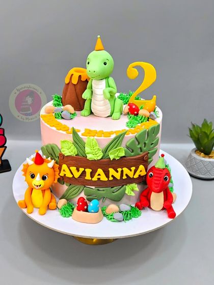 A cute dinosaur-themed cake for Avianna's 2nd birthday, featuring friendly fondant dinosaurs, a volcano, and jungle leaves.