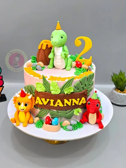 A cute dinosaur-themed cake for Avianna's 2nd birthday, featuring friendly fondant dinosaurs, a volcano, and jungle leaves.