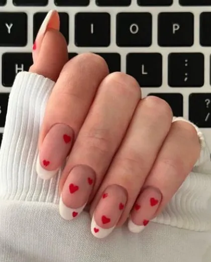 A sweet French manicure with classic white tips and small red hearts floating over the natural nail base.