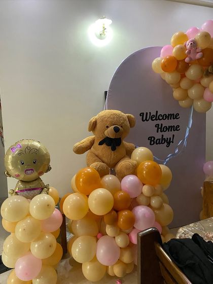 A close-up of the 'Welcome Home Baby' decor, showing the teddy bear and baby-themed foil balloon nestled in the pastel balloon arrangement.