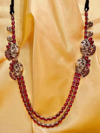 The red stone and silver peacock necklace displayed against a warm, golden fabric, highlighting the rich color of the stones and the intricate silverwork.