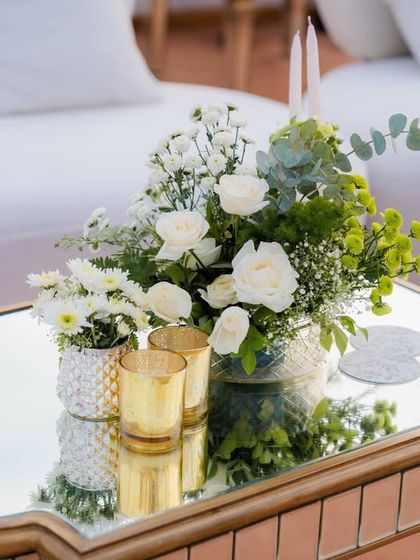 A chic centerpiece on a mirrored table, featuring a simple arrangement of white roses and greenery in a silver vase. The reflection on the table adds a layer of depth and sophistication to the minimalist design.