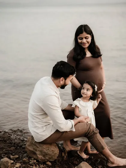 A beautiful family portrait by the lake. The parents and their daughter share a quiet moment together, all focused on the new life they are waiting for.