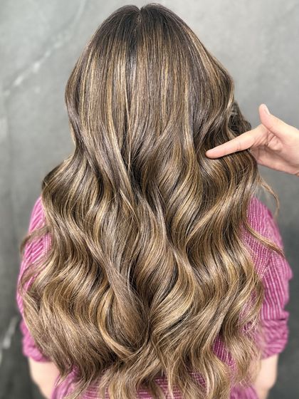 A stylist pointing to the perfectly blended highlights, showcasing the technique and the stunning result.