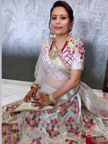 A full seated portrait showing the complete look. The makeup is subtle yet polished, allowing the intricate details of her beautiful lehenga to shine.