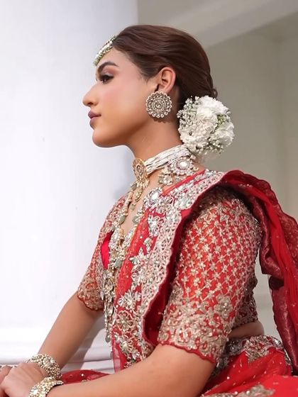 A close-up on the hairstyle, featuring a classic bun adorned with white carnations, adding a soft, romantic touch to the bold red outfit.