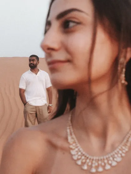 A beautiful portrait using a shallow depth of field, with the bride's serene expression in focus while the groom stands thoughtfully in the background of the Dubai desert.