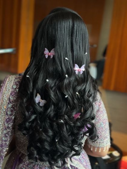 A whimsical and dreamy open hairstyle with soft curls, decorated with delicate butterfly clips and pearls.