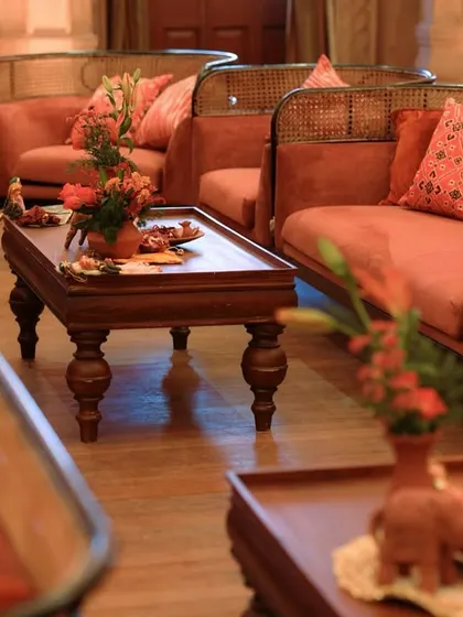 A lounge area with rustic wooden and cane furniture, upholstered in a warm terracotta fabric with patterned cushions, creating a comfortable and culturally rich atmosphere.