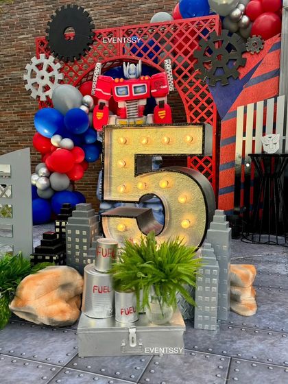 Another angle of the Transformers setup, showing the lit-up marquee number "5" and custom props like fuel cans and cityscape cutouts. Every detail is designed to immerse kids in the Autobots' world.