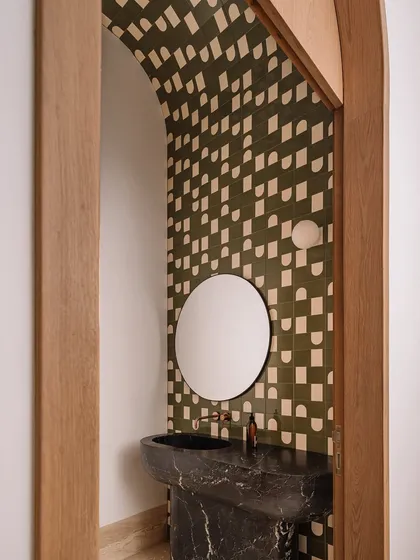 This bathroom is all about playful geometry, with pixelated mosaic tiles in earthy tones creating a dynamic pattern on the floor and walls. The design is anchored by a sculptural pink marble vanity, creating a space that is bold and full of personality.