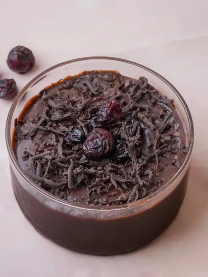 A rich chocolate mousse in a glass, topped with chocolate shavings and dried cranberries. The light background contrasts beautifully with the dark dessert, making it look decadent and appealing.