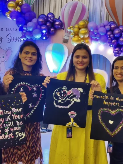 A group of friends displays their finished tote bags with sweet messages and drawings, a collective gift for the mom-to-be.