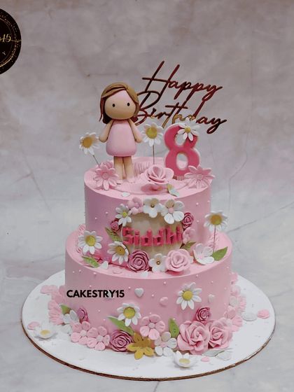 A beautiful two-tier floral doll cake. This choco-vanilla cake is decorated in shades of pink and features a sweet doll topper, surrounded by a garden of delicate, multi-colored sugar flowers.