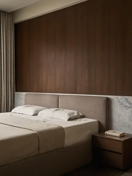 The bed in the master bedroom is set against a full-height walnut veneer wall, with a low Carrara marble wainscoting that wraps around the room. The custom bed and side tables are designed to be minimal and unobtrusive, focusing on material richness.