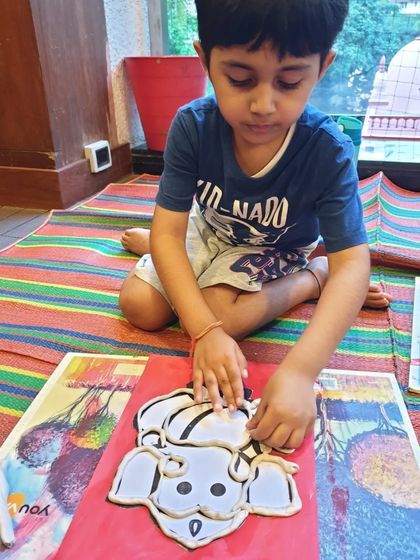 A young boy making a Ganesha idol using clay on a red board. This is a wonderful tactile activity that connects children to the festive tradition.