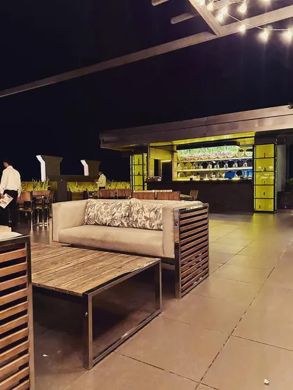 This image shows the relationship between the lounge seating and the bar area in the rooftop cafe. The custom-made sofa and coffee table, crafted from wood and metal, reflect the industrial-chic aesthetic of the space.