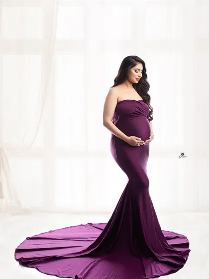 A simple yet elegant portrait in a fitted, floor-length purple gown. The clean background and soft lighting put all the focus on the beautiful shape of the baby bump and the serene expression of the mother-to-be.