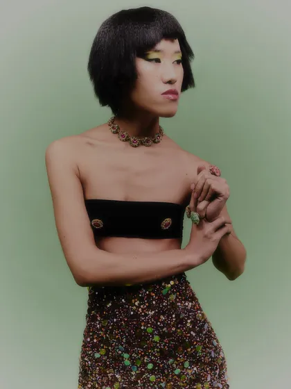 A portrait that highlights the jeweled choker and the model's playful expression. The styling is confident and fashion-forward.