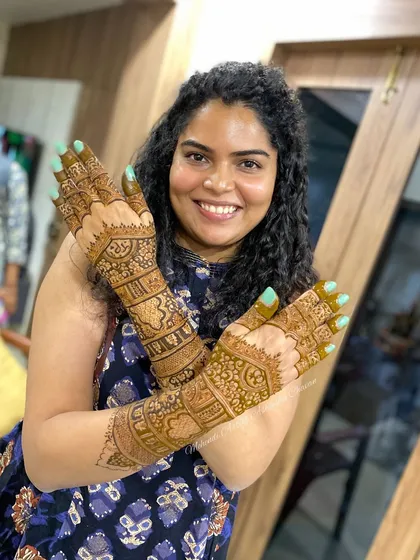 A happy engagement bride showing off her intricate mehendi. The design covers her hands and arms in beautiful, traditional patterns.