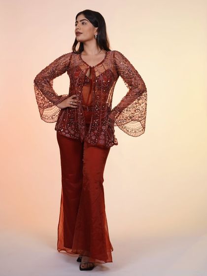 A full-length view of the rust-colored Indo-Western set, with its flared pants and beautifully embellished corset top and jacket.