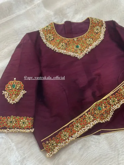 A rich wine-colored blouse featuring a grand, jewellery-inspired neckline and sleeve embroidery with red and green stones.
