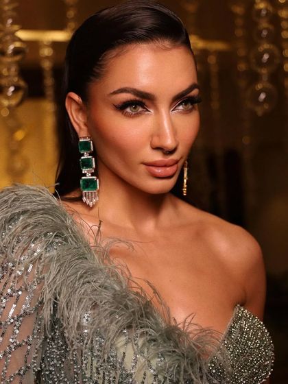 A close-up on a model with a dramatic winged eyeliner and statement emerald earrings.