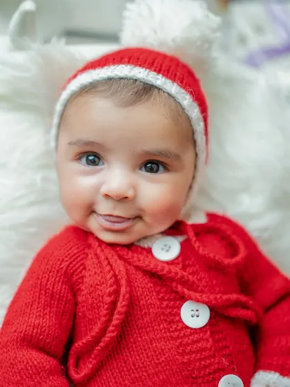 A close-up of a newborn's sweet face during a Christmas shoot. The soft, knitted Santa outfit keeps the baby cozy and adds to the festive charm.