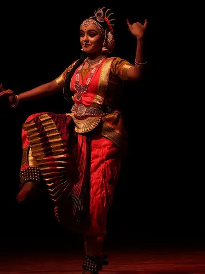 A solo dancer in a striking pose, her form beautifully illuminated against the dark stage at the Sadhana festival.