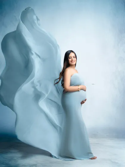 A sweep of sky blue. This portrait uses a flowing blue fabric to create a sense of movement and grace, beautifully highlighting the baby bump.