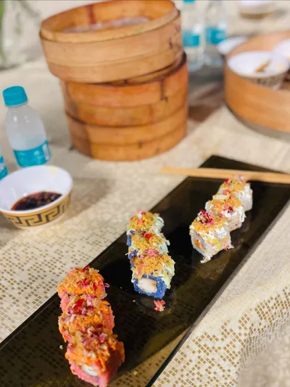 A table setting featuring freshly made sushi, with bamboo steamers in the background, hinting at the variety of Pan-Asian food available.