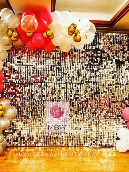 A glamorous photo backdrop featuring a gold and silver shimmer wall framed by a red, white, and gold balloon garland. It's perfect for any chic celebration.