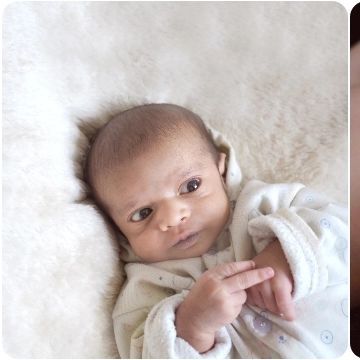 An awake newborn looking thoughtfully at their own tiny fingers.